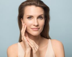 A woman smiling and looking at the camera while framing the side of her face with her hands