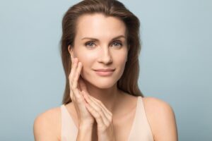 A woman smiling and looking at the camera while framing the side of her face with her hands